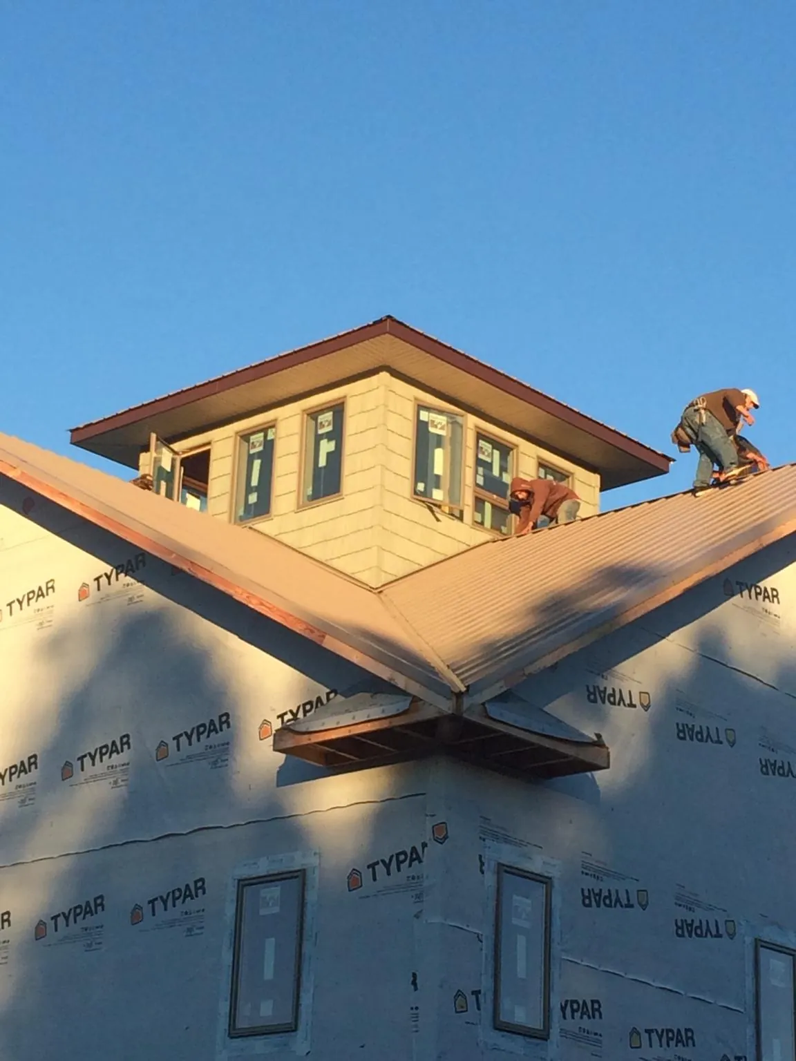 Roofers working around a rooftop cupola on a new metal roof at sunset — Roof Waterproofing in Newcastle by Roofing Brothers